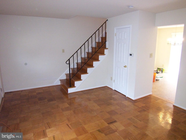 stairway featuring an inviting chandelier and dark parquet flooring