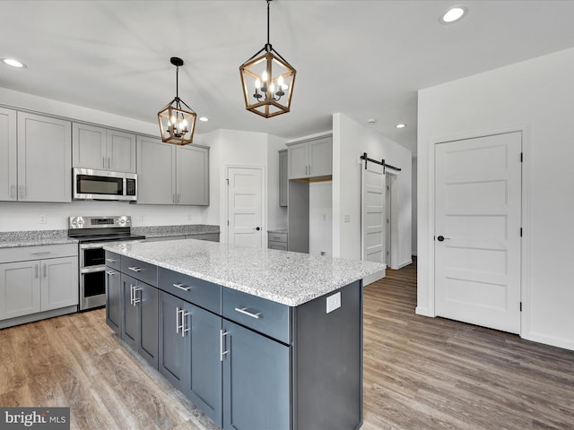 kitchen featuring gray cabinetry, appliances with stainless steel finishes, light hardwood / wood-style floors, a barn door, and decorative light fixtures