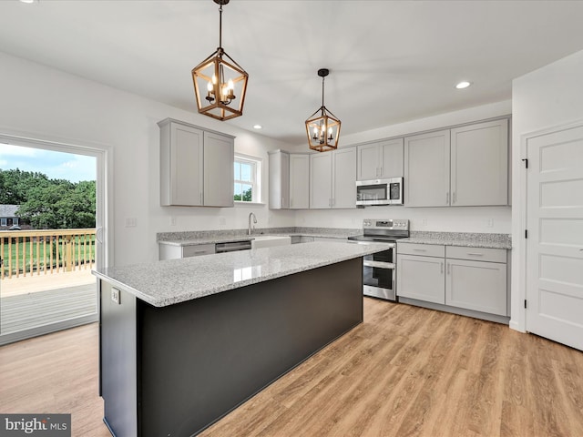 kitchen featuring appliances with stainless steel finishes, light hardwood / wood-style floors, pendant lighting, gray cabinetry, and light stone countertops