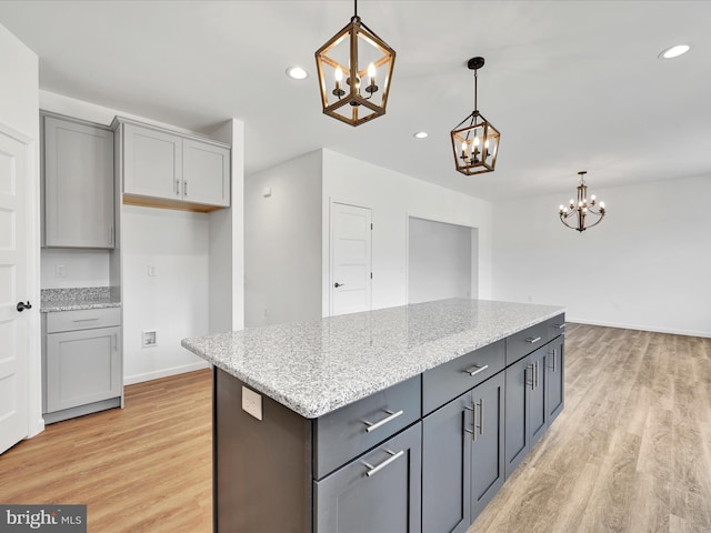 kitchen featuring decorative light fixtures, light stone counters, a center island, gray cabinets, and light wood-type flooring