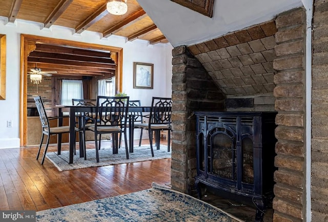 dining space with dark wood-type flooring, ceiling fan, a stone fireplace, wooden ceiling, and lofted ceiling with beams