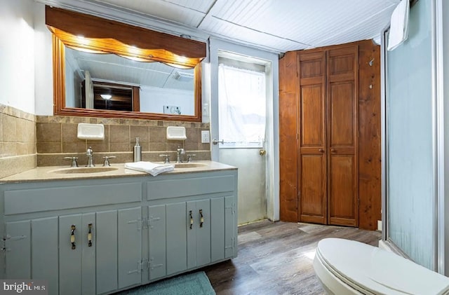 bathroom with double sink vanity, backsplash, wood-type flooring, and toilet