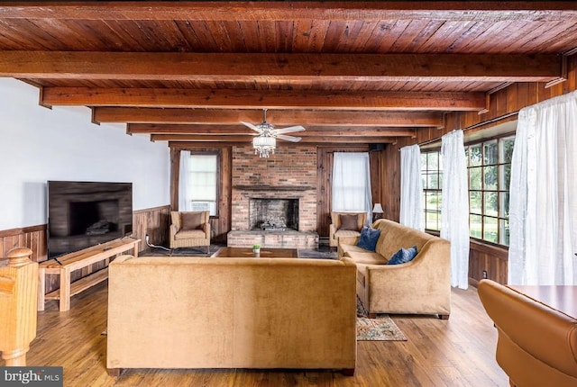 living room with ceiling fan, beamed ceiling, a brick fireplace, wood ceiling, and hardwood / wood-style flooring