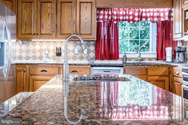 kitchen featuring stainless steel fridge, sink, dark stone counters, dishwashing machine, and tasteful backsplash