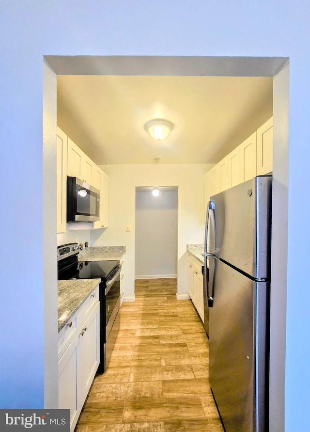 kitchen featuring white cabinets, appliances with stainless steel finishes, light stone counters, and light wood-type flooring