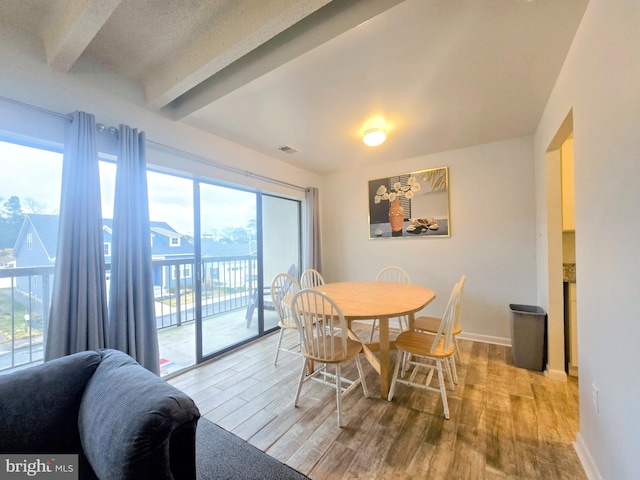 dining room featuring light wood-type flooring, a wealth of natural light, and beamed ceiling