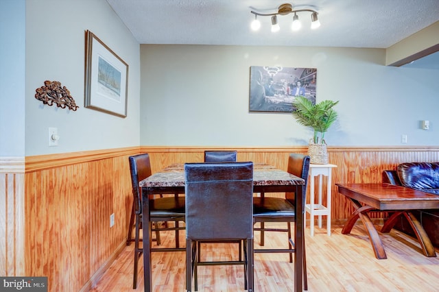 dining space featuring rail lighting, light hardwood / wood-style floors, and a textured ceiling