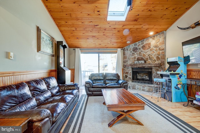 living room with a stone fireplace, vaulted ceiling with skylight, hardwood / wood-style floors, and plenty of natural light