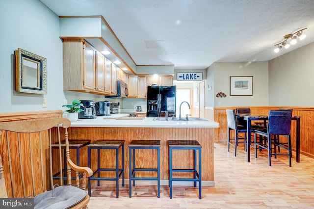 kitchen with a breakfast bar area, stainless steel appliances, a textured ceiling, kitchen peninsula, and light hardwood / wood-style flooring