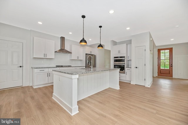 kitchen featuring wall chimney exhaust hood, a kitchen island with sink, white cabinets, and light hardwood / wood-style flooring