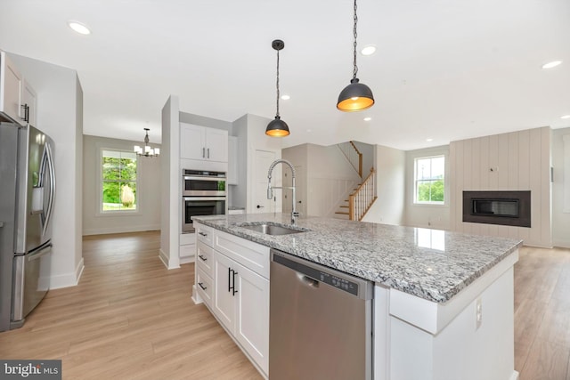 kitchen featuring light hardwood / wood-style floors, white cabinets, stainless steel appliances, a kitchen island with sink, and a fireplace