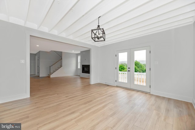 unfurnished living room featuring a notable chandelier, beam ceiling, french doors, and light hardwood / wood-style flooring