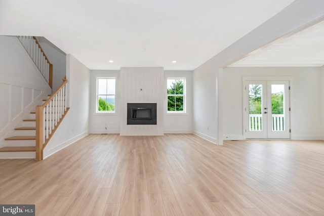 unfurnished living room featuring light hardwood / wood-style flooring, french doors, and a large fireplace