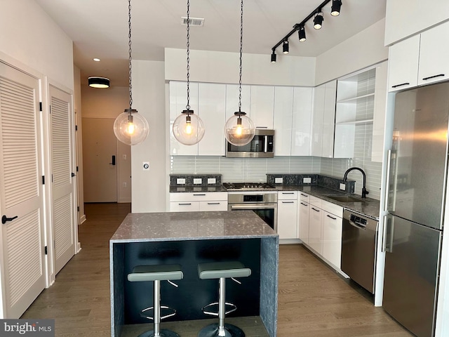 kitchen featuring dark wood-type flooring, appliances with stainless steel finishes, sink, dark stone countertops, and tasteful backsplash