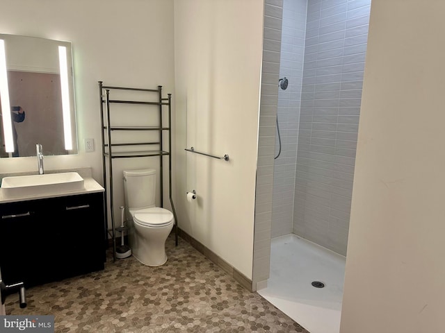 bathroom featuring tile floors, toilet, vanity, and a tile shower