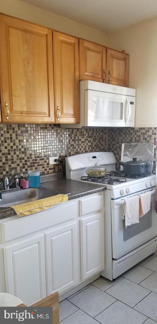 kitchen with backsplash, light tile floors, white appliances, and sink