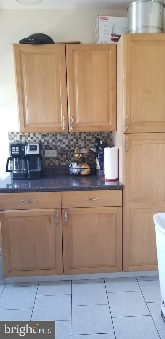 kitchen with light tile floors, dark stone counters, and backsplash