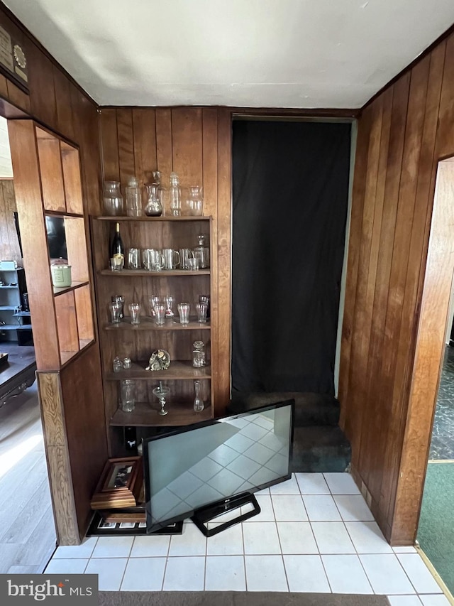 bar featuring light tile floors, wood walls, and dark brown cabinets