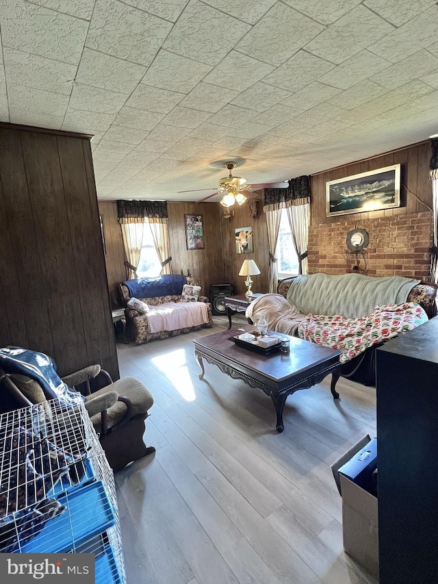 living room featuring wooden walls, ceiling fan, and a healthy amount of sunlight