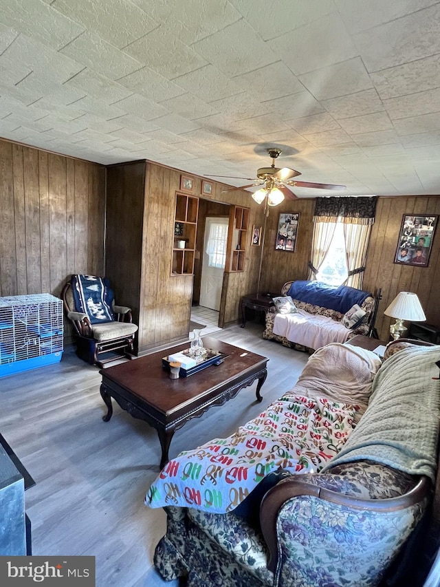 living room featuring light hardwood / wood-style floors, wooden walls, and ceiling fan