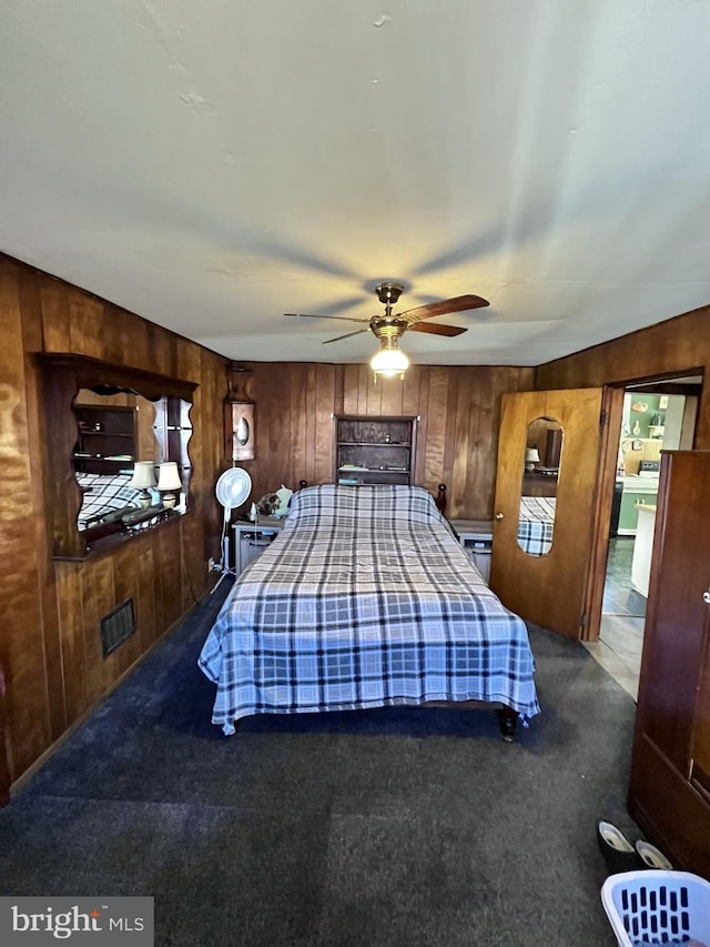 bedroom featuring wooden walls, ceiling fan, and carpet