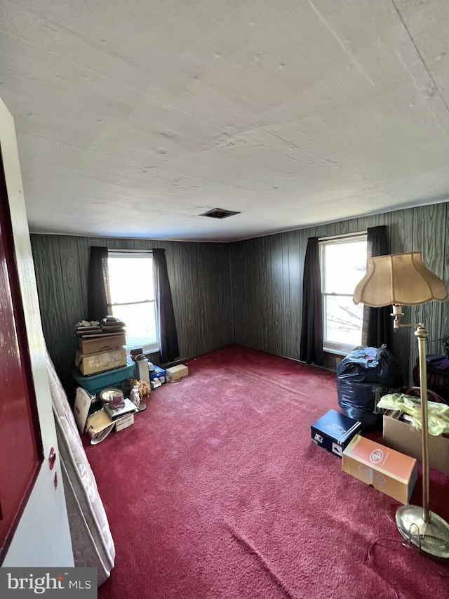 interior space with dark colored carpet, wood walls, and a healthy amount of sunlight