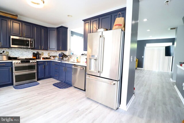 kitchen with light wood-type flooring, backsplash, sink, blue cabinets, and appliances with stainless steel finishes