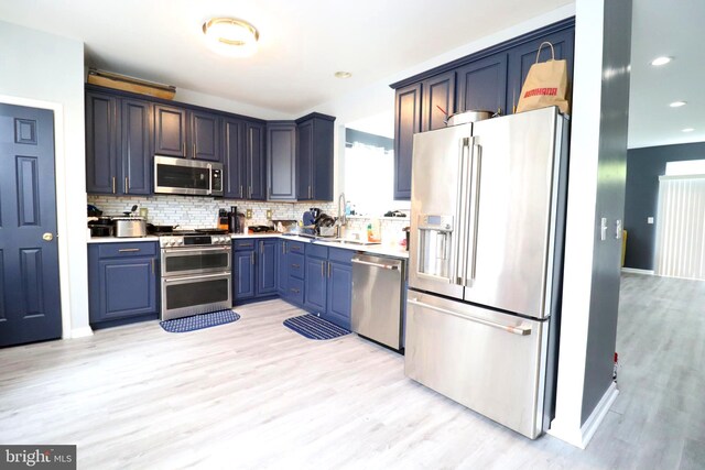 kitchen featuring light wood-type flooring, stainless steel appliances, tasteful backsplash, and blue cabinetry