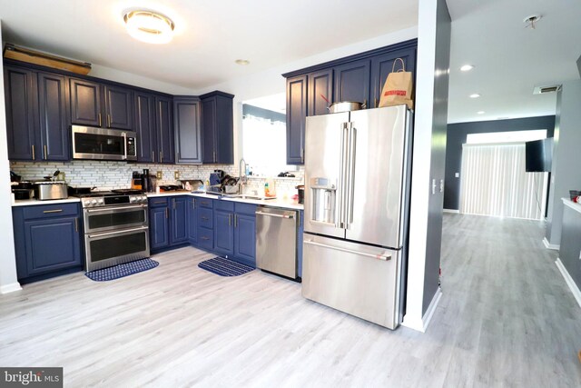 kitchen with blue cabinetry, light hardwood / wood-style flooring, stainless steel appliances, sink, and decorative backsplash