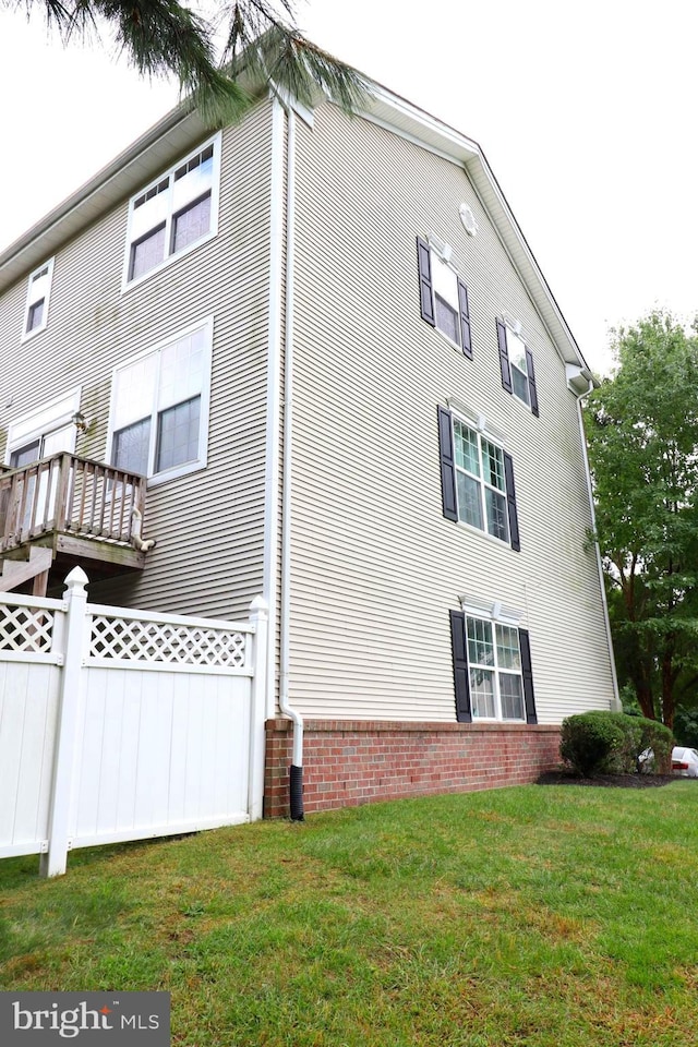 view of property exterior with brick siding, a lawn, and fence