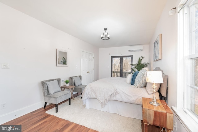 bedroom featuring access to exterior, a wall mounted air conditioner, wood-type flooring, and french doors