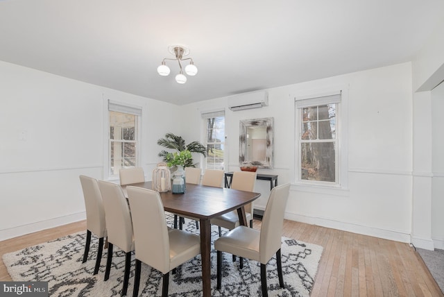 dining room with a wall unit AC, light hardwood / wood-style floors, a healthy amount of sunlight, and a chandelier