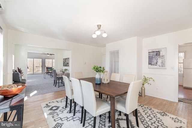 dining space featuring light carpet and ceiling fan with notable chandelier