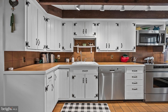 kitchen with appliances with stainless steel finishes, tasteful backsplash, beamed ceiling, sink, and white cabinets