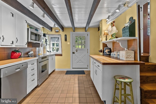 kitchen featuring stainless steel appliances, backsplash, light tile flooring, white cabinetry, and beamed ceiling