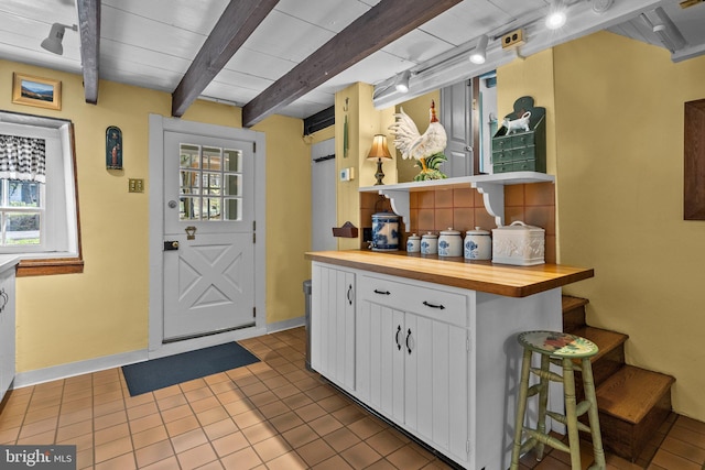 kitchen featuring light tile flooring, beamed ceiling, a breakfast bar, white cabinetry, and butcher block countertops