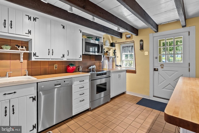 kitchen with beam ceiling, stainless steel appliances, white cabinets, and tasteful backsplash