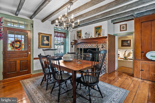 dining area with beam ceiling, a tiled fireplace, a chandelier, and light hardwood / wood-style flooring