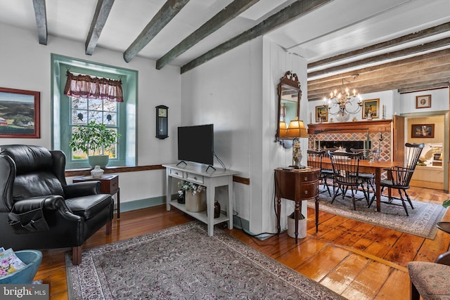 living room with an inviting chandelier, beam ceiling, hardwood / wood-style flooring, and a fireplace