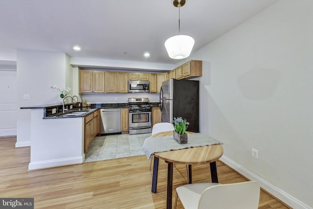 kitchen with kitchen peninsula, stainless steel appliances, sink, pendant lighting, and light hardwood / wood-style floors