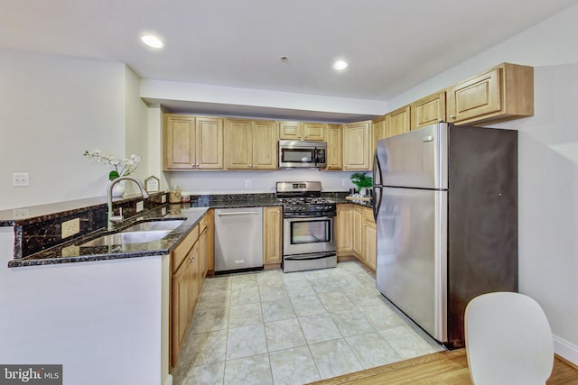 kitchen featuring dark stone counters, sink, light wood-type flooring, appliances with stainless steel finishes, and kitchen peninsula