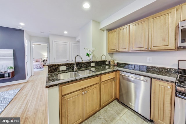 kitchen featuring kitchen peninsula, appliances with stainless steel finishes, dark stone counters, and sink