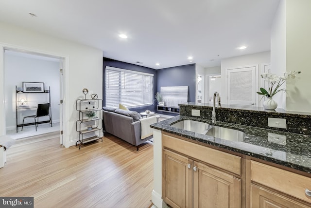 kitchen with sink, dark stone counters, and light wood-type flooring