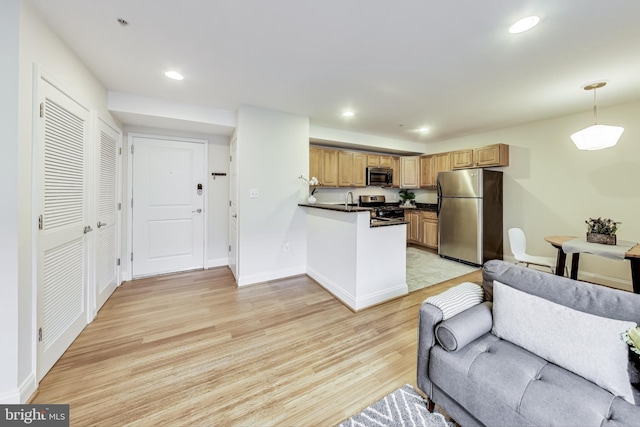 kitchen featuring sink, hanging light fixtures, light wood-type flooring, kitchen peninsula, and stainless steel appliances