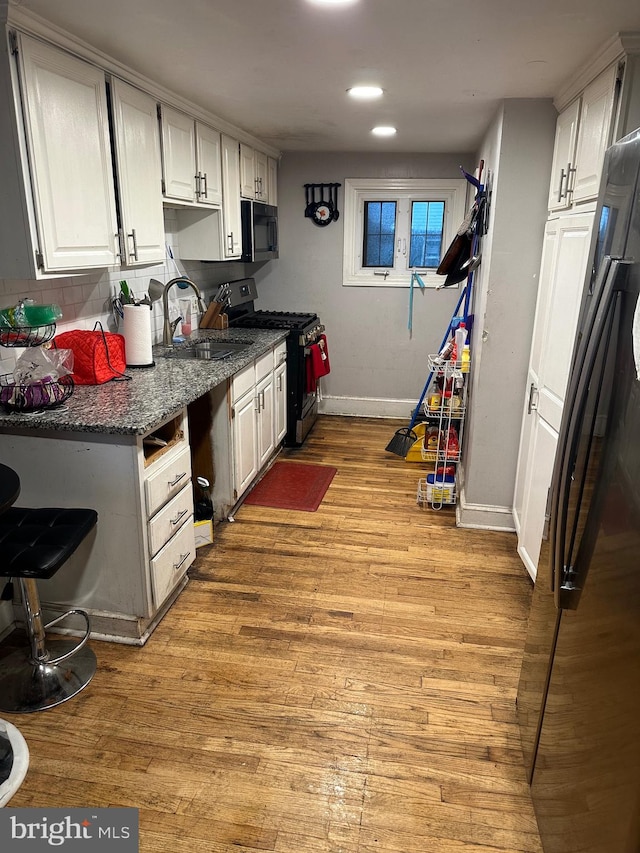 kitchen featuring dark stone countertops, light hardwood / wood-style floors, white cabinetry, appliances with stainless steel finishes, and backsplash