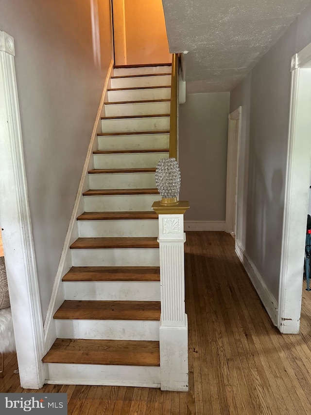 staircase with wood-type flooring and a textured ceiling