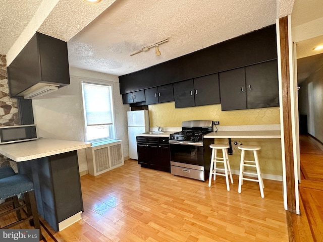 kitchen featuring stainless steel range with gas cooktop, a kitchen bar, a textured ceiling, and light hardwood / wood-style floors