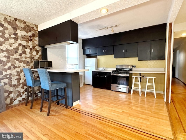 kitchen featuring a breakfast bar, white fridge, light hardwood / wood-style floors, a textured ceiling, and stainless steel range with gas cooktop