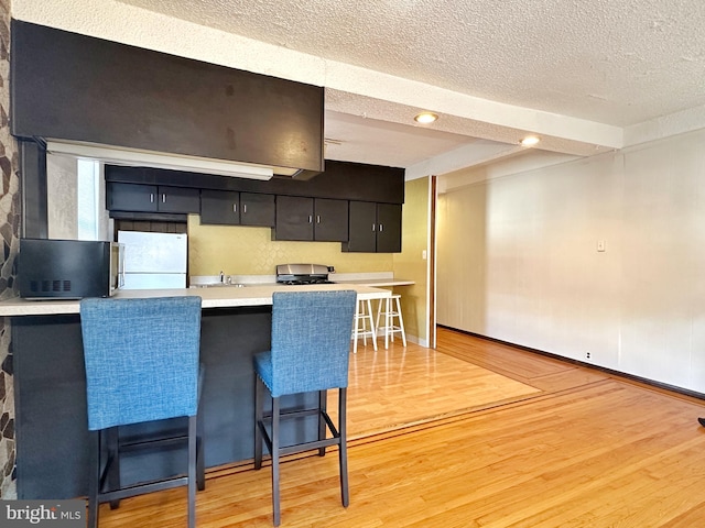 kitchen with range, white fridge, a kitchen breakfast bar, light hardwood / wood-style flooring, and a textured ceiling