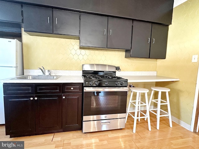 kitchen featuring white fridge, dark brown cabinets, light wood-type flooring, sink, and stainless steel gas range oven